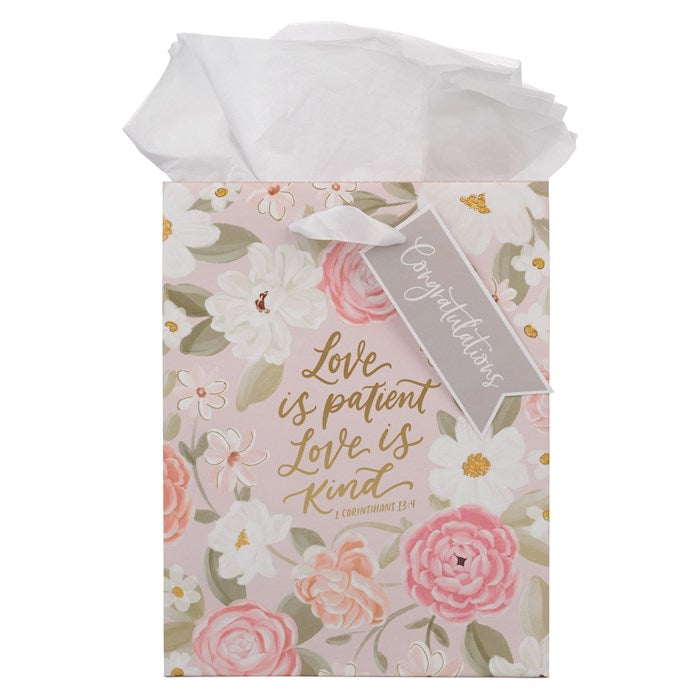 Floral gift bag with 'Love is patient, love is kind' text and white tissue paper.