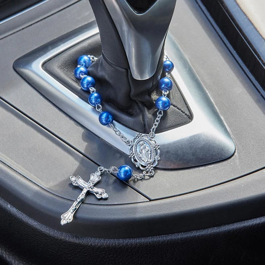 A blue beaded rosary with a silver crucifix and medallion resting on a car gear shift console.