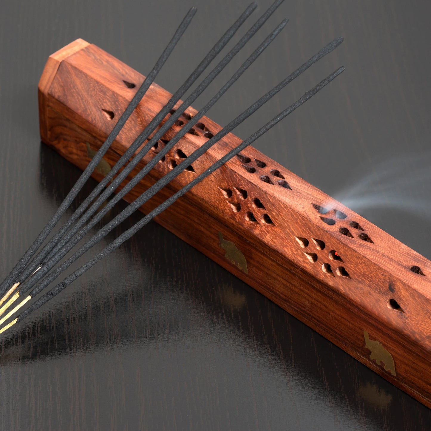 Wooden incense holder with burning incense sticks on a dark background
