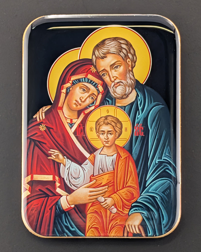 Decorative wooden magnet with religious artwork of a family, likely the Holy Family, on a dark background.
