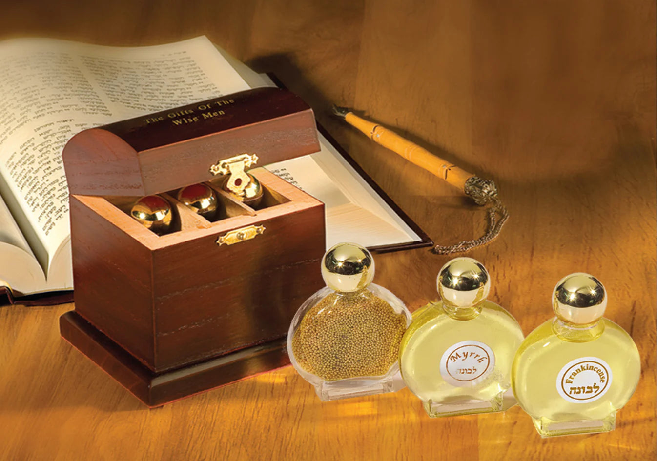 Three small bottles with gold caps and a wooden box on a wooden surface with an open book and quill pen.