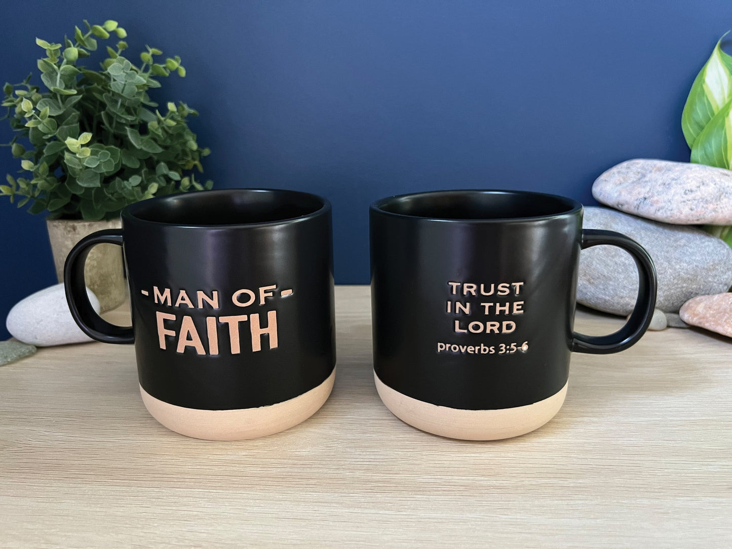 Two black mugs with motivational phrases on a wooden surface against a blue wall.