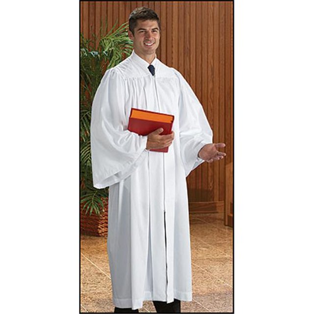 Man wearing a white robe holding a red and orange book in front of a wooden paneled wall.