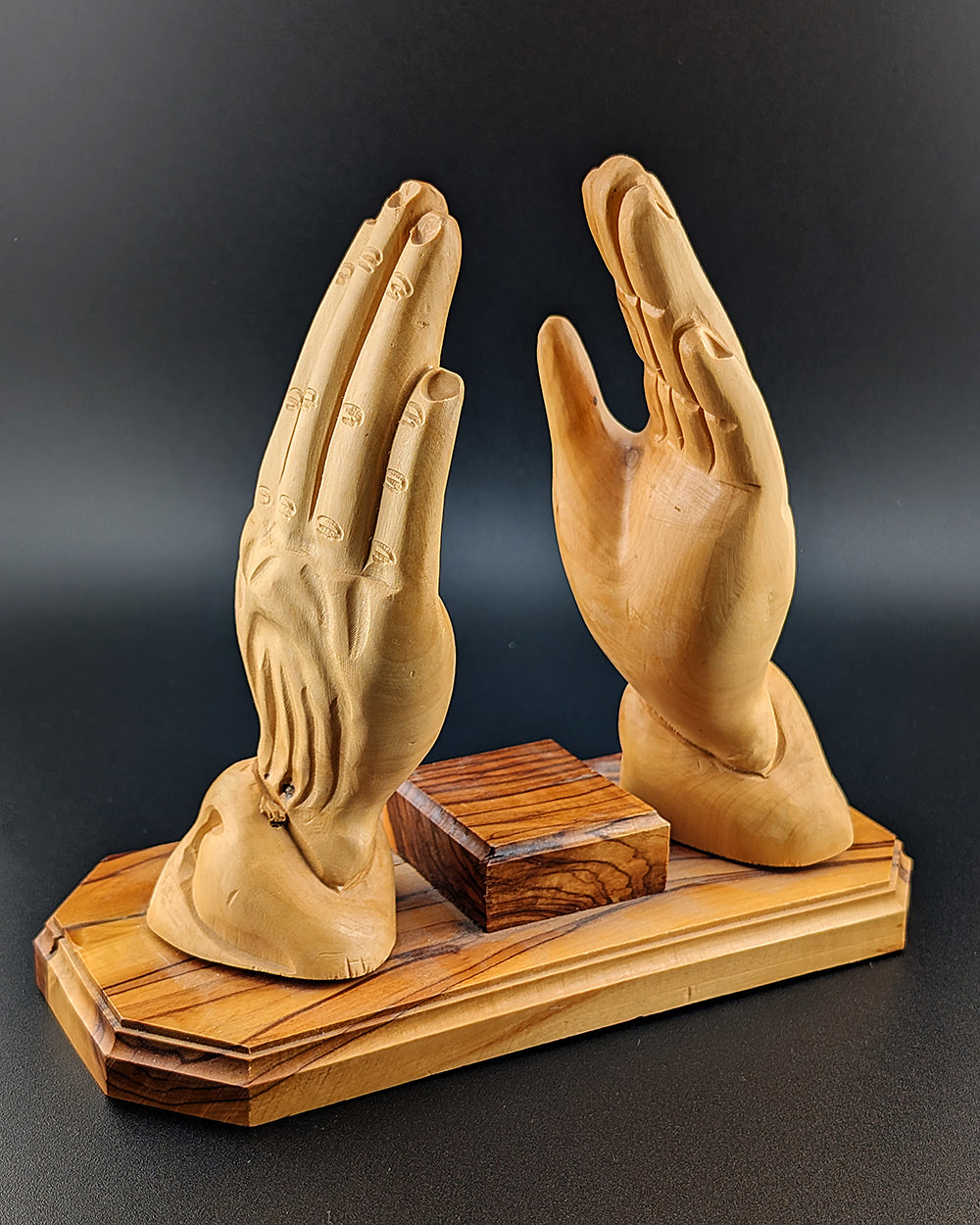 Wooden sculpture of two hands on a wooden base against a dark background