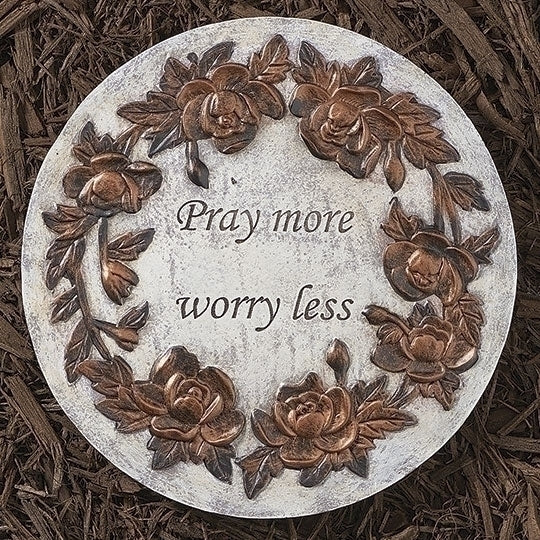 A circular garden stone with a floral design and the message 'Pray more worry less' in the center.