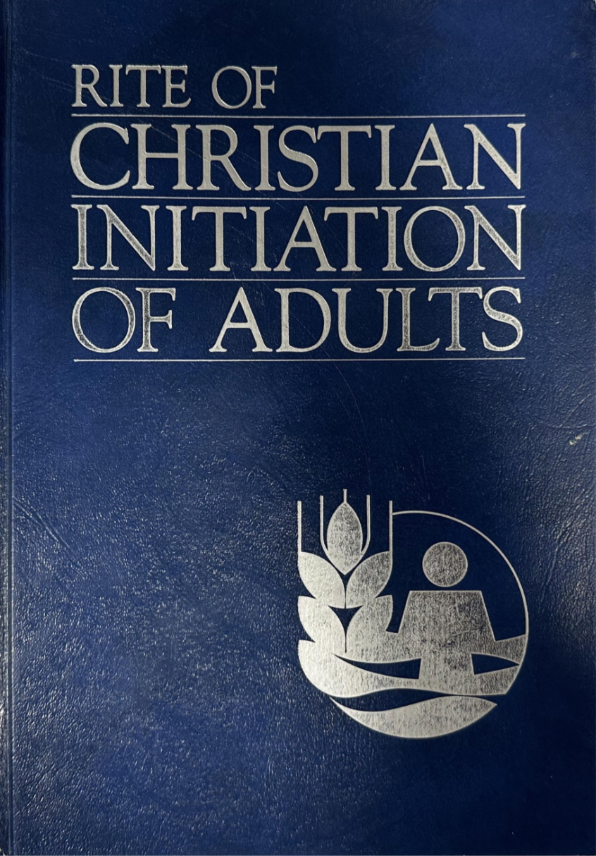 Blue book titled 'Rite of Christian Initiation of Adults' with a symbol on a dark blue background