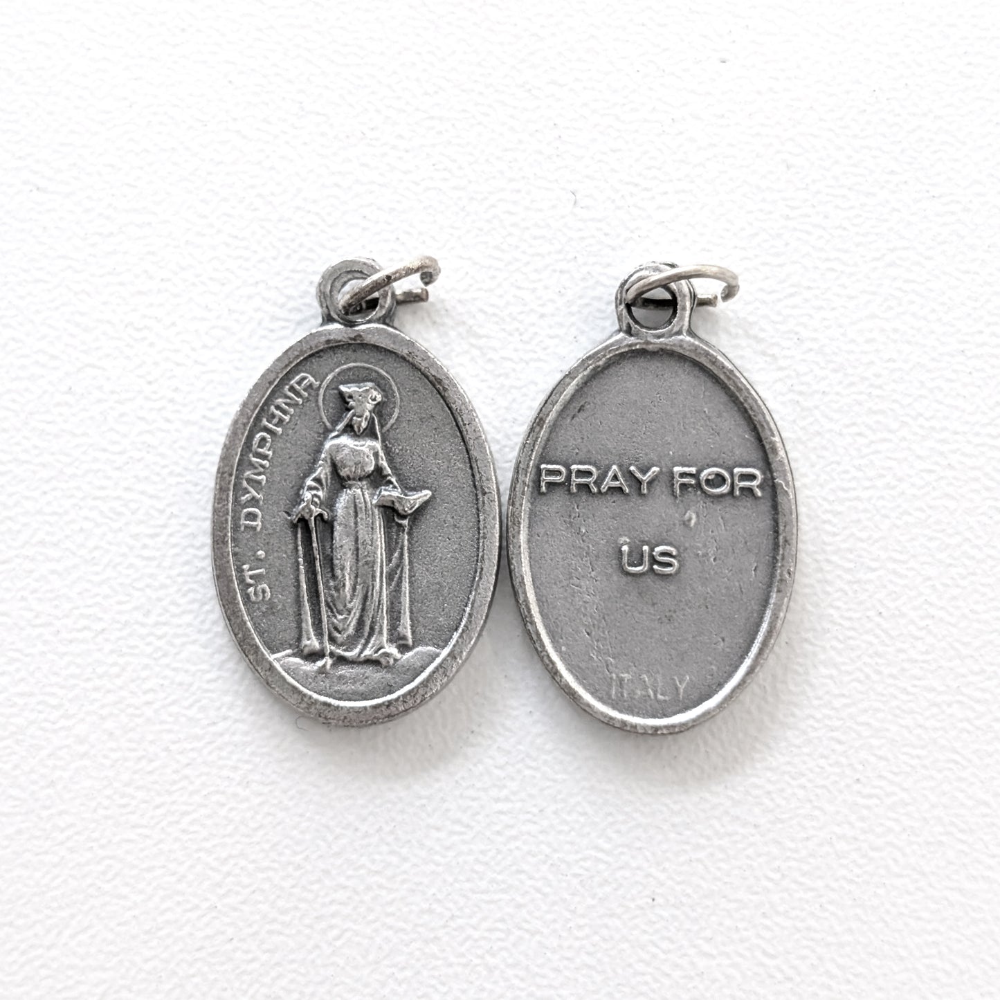 Silver religious pendant with a figure and 'Pray for Us' text on a white background
