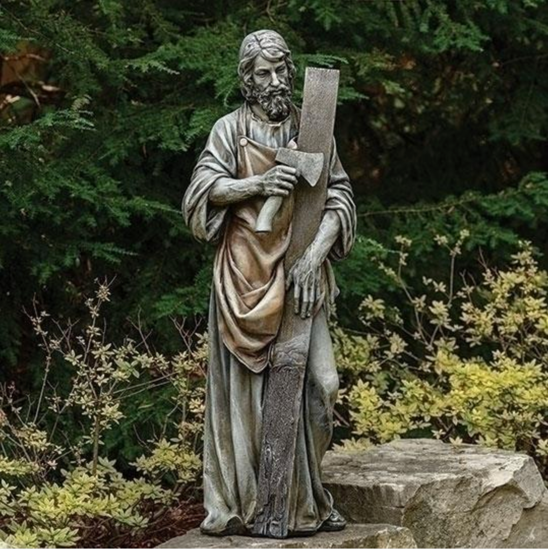Statue of a religious figure holding a book in a garden setting