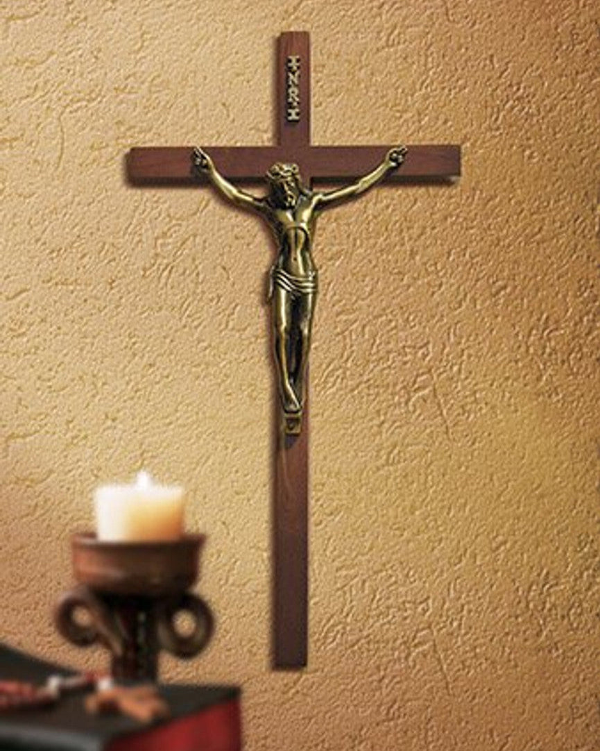 Wooden cross with a bronze figure of Jesus on a beige wall, next to a candle holder with a lit candle.