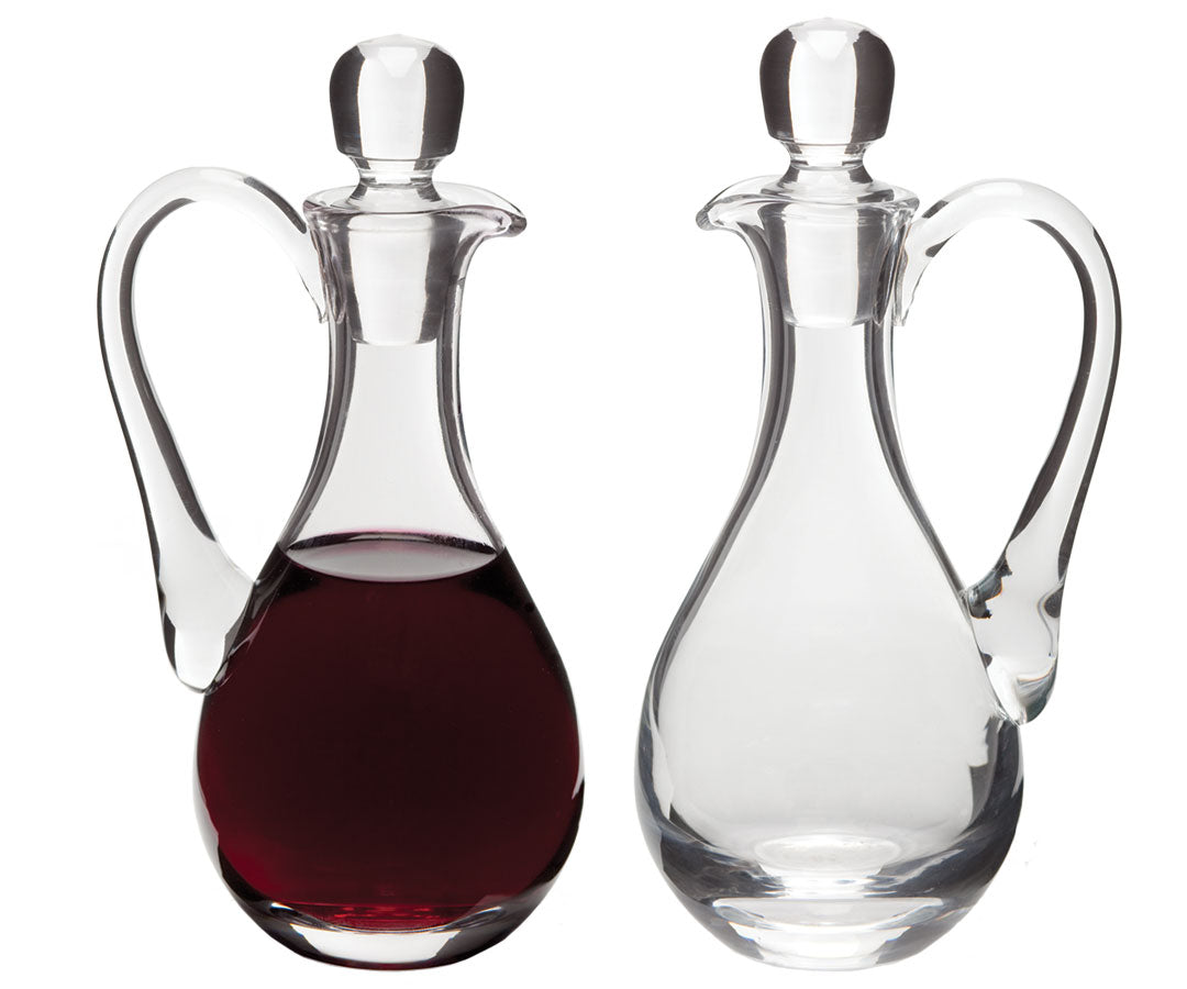 Two clear glass cruets with sweeping handles and tapered necks, one filled with red wine, the other with water.