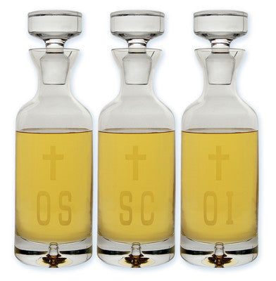 Set of three clear glass decanters with metal caps, each engraved with a different letter 'OI', 'OS', 'SC' in a yellow-toned liquid, typically used for storing holy oil.