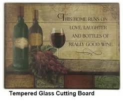 A tempered glass cutting board with a wine-themed graphic that includes two wine glasses, a bottle of wine, and text that reads 'This Home Runs on Love Laughter and Bottles of Really Good Wine'.