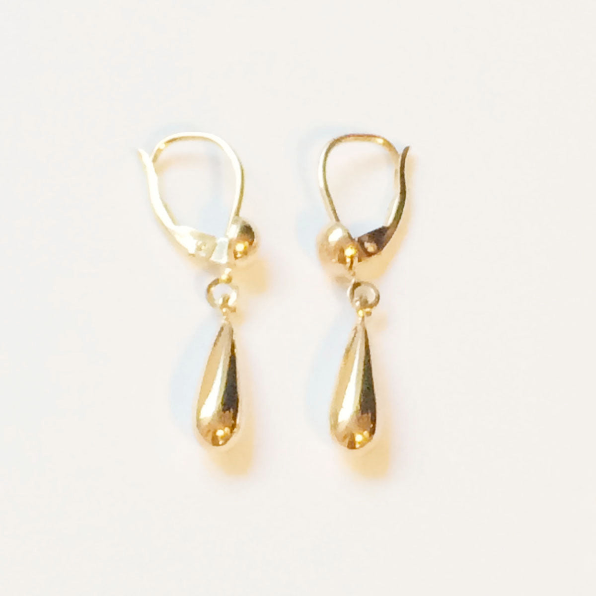 Gold teardrop earrings on a light gray background