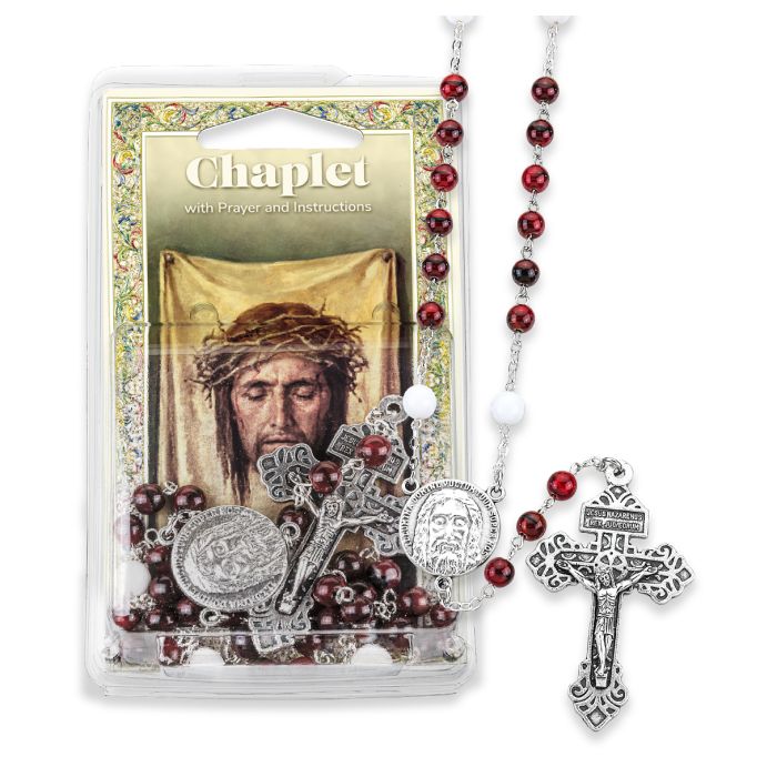 A silver oxidized Holy Face medal and a Pardon Crucifix with red beads, a small prayer card, and a pamphlet on the Chaplet, all displayed in a clear box.