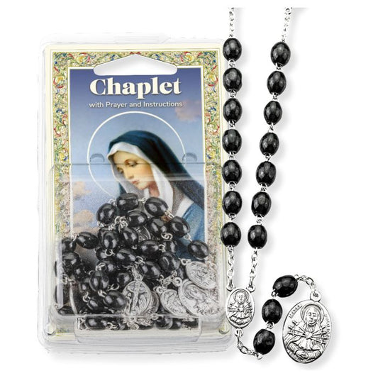 A black beaded rosary chaplet with a pewter centerpiece, displayed in clear plastic packaging, including a laminated Holy card.