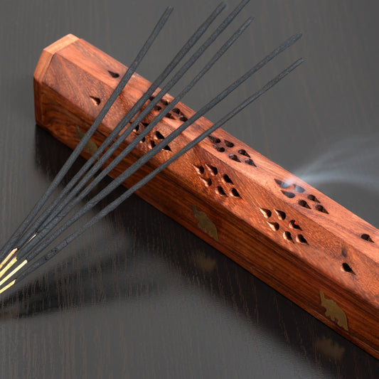 Wooden incense holder with burning incense sticks on a dark background