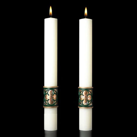 Two white candles with decorative green holders on a black background