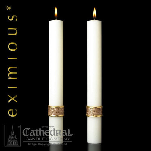 Two white candles with gold bands on a black background, featuring the Eximious logo and Cathedral Candle Company branding.