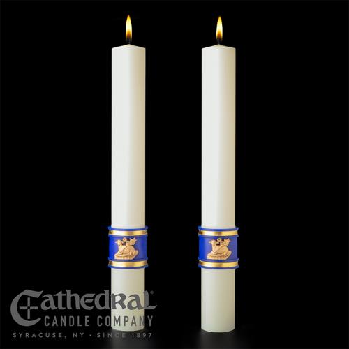 Two white candles with blue and gold bands on a black background, featuring the Cathedral Candle Company logo.