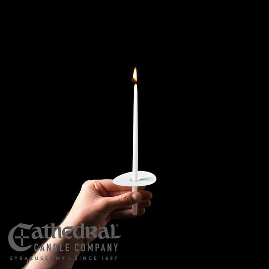 A hand holding a lit 9-inch white taper candle with a paper bobech on a black background.