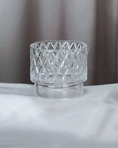 Clear glass candle holder on a white surface with a neutral background