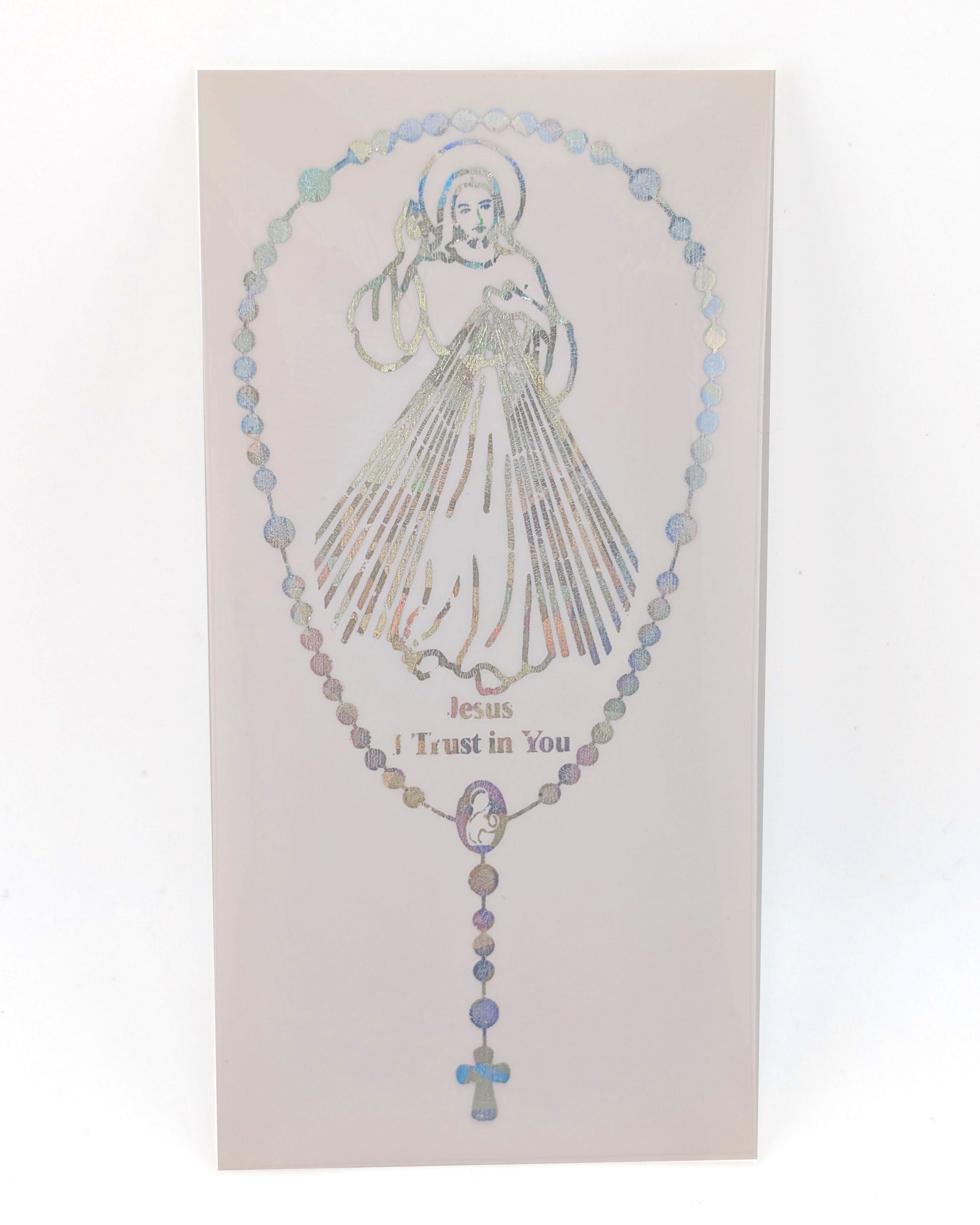 A rectangular religious card or plaque featuring a rosary design with a silver-toned illustration of Jesus and the words 'Jesus Trust in You.' The rosary beads have a subtle iridescent, holographic finish that shifts between blue, purple, and gold tones.
