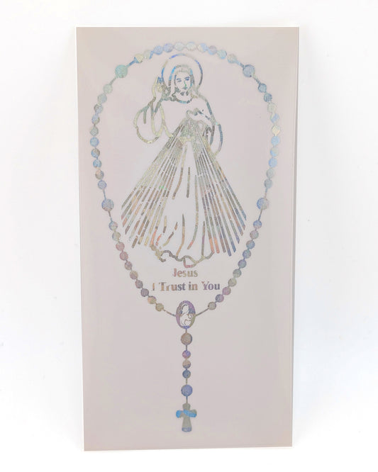 A rectangular religious card or plaque featuring a rosary design with a silver-toned illustration of Jesus and the words 'Jesus Trust in You.' The rosary beads have a subtle iridescent, holographic finish that shifts between blue, purple, and gold tones.