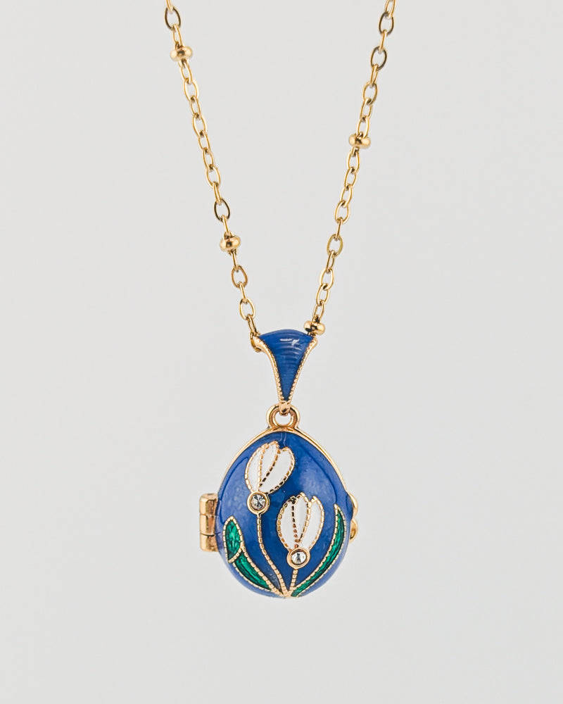 Blue locket with floral design on a gold chain against a light gray background