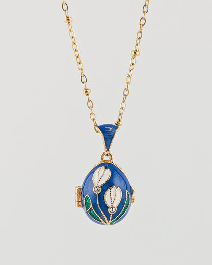 Blue locket with floral design on a gold chain against a light gray background