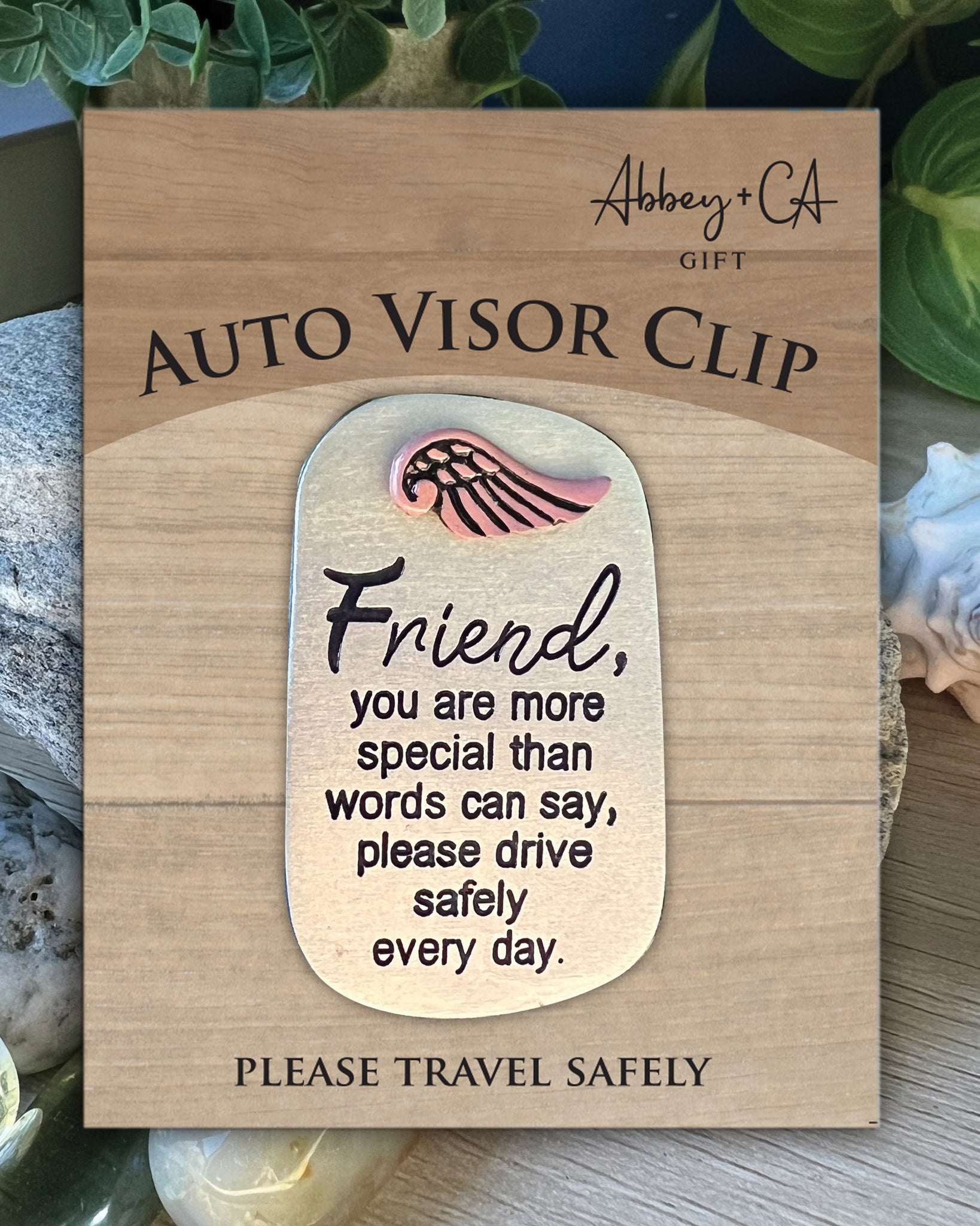 Wooden auto visor clip with a sentimental message on a wooden card, surrounded by seashells and greenery.