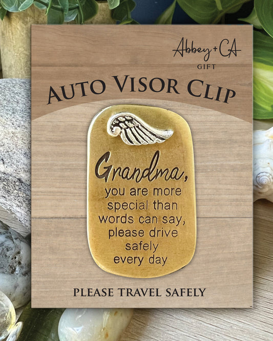 Auto visor clip with engraved message on a wooden card, surrounded by seashells and greenery.