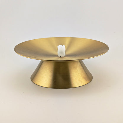 Gold metal cake stand with a white candle on a light gray background