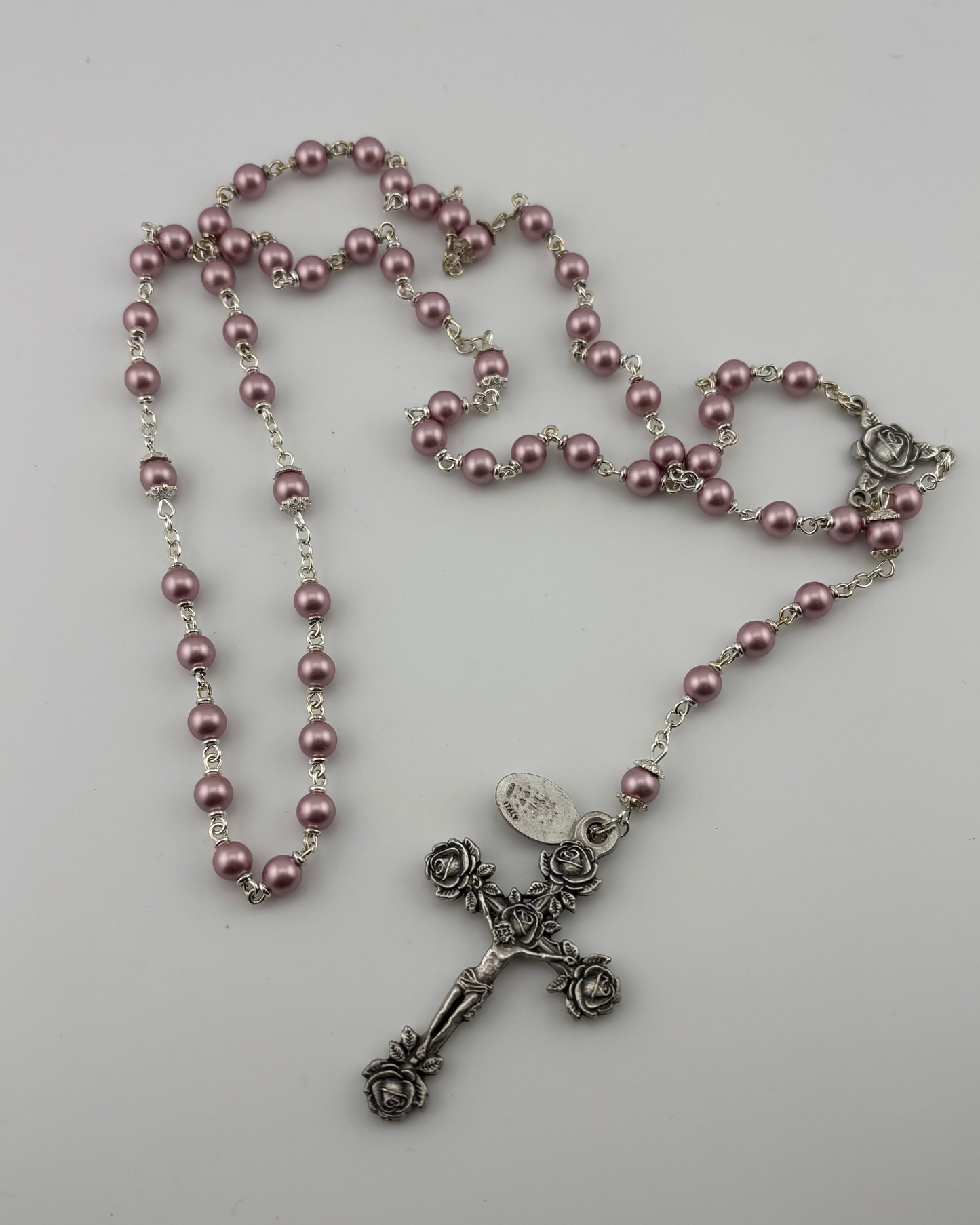 Pink rosary with a silver cross on a light gray background