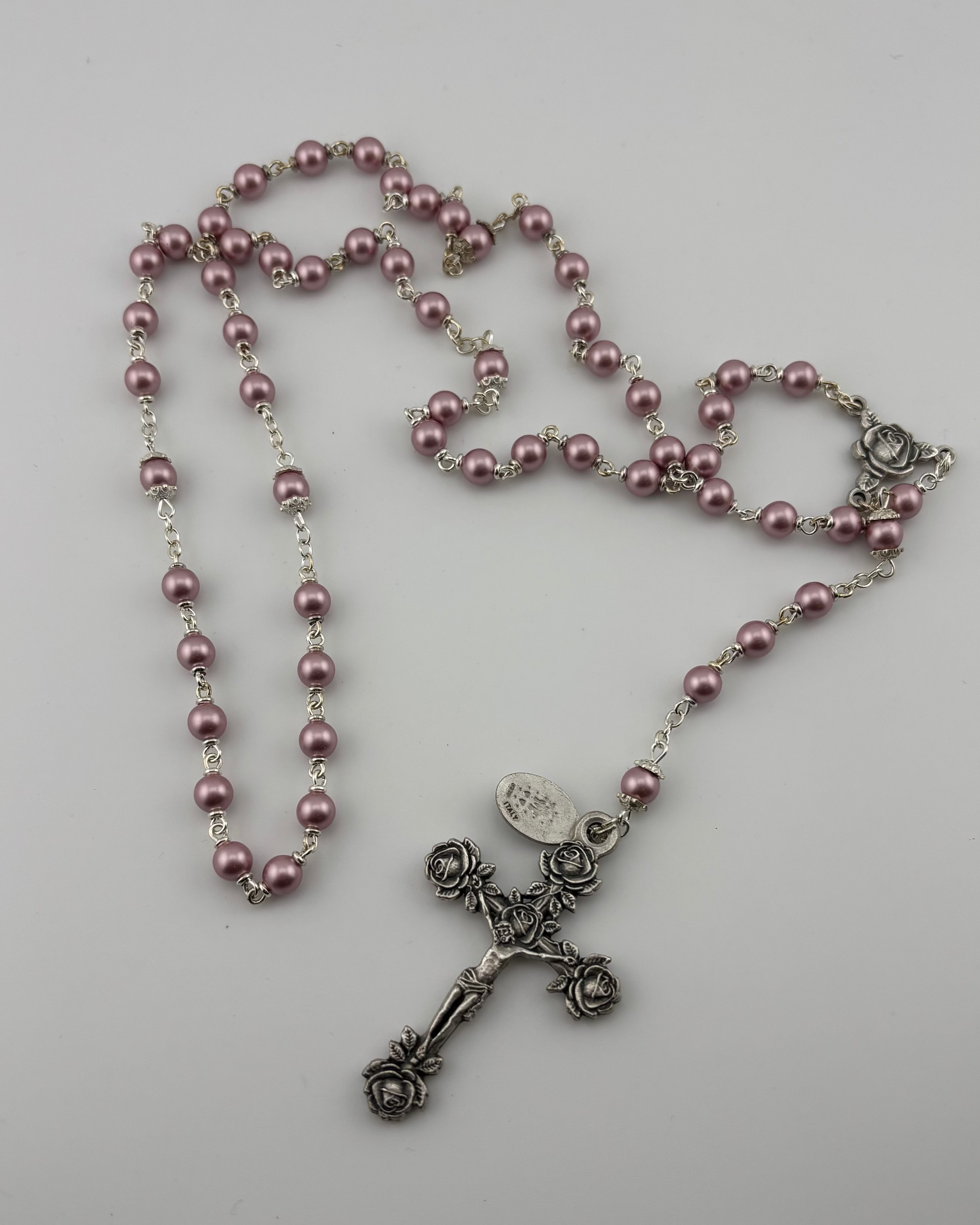 Pink rosary with a silver cross on a light gray background