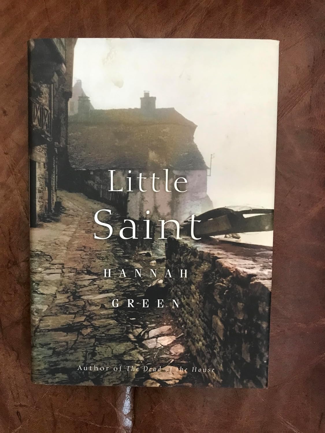 Book cover of 'Little Saint' by Hannah Green on a wooden surface