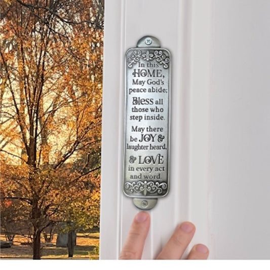 A metal wall plaque with a home blessing message, attached to a white door, featuring a silver tone finish.
