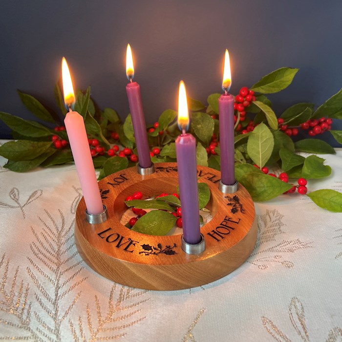 Wooden advent candle holder with lit candles on a decorative tablecloth.