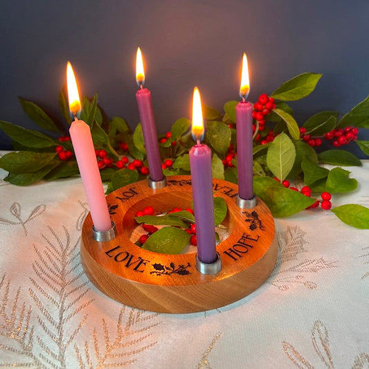 Wooden advent candle holder with lit candles on a decorative tablecloth.