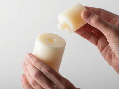 Hand holding a small candle and a piece of wax against a light background