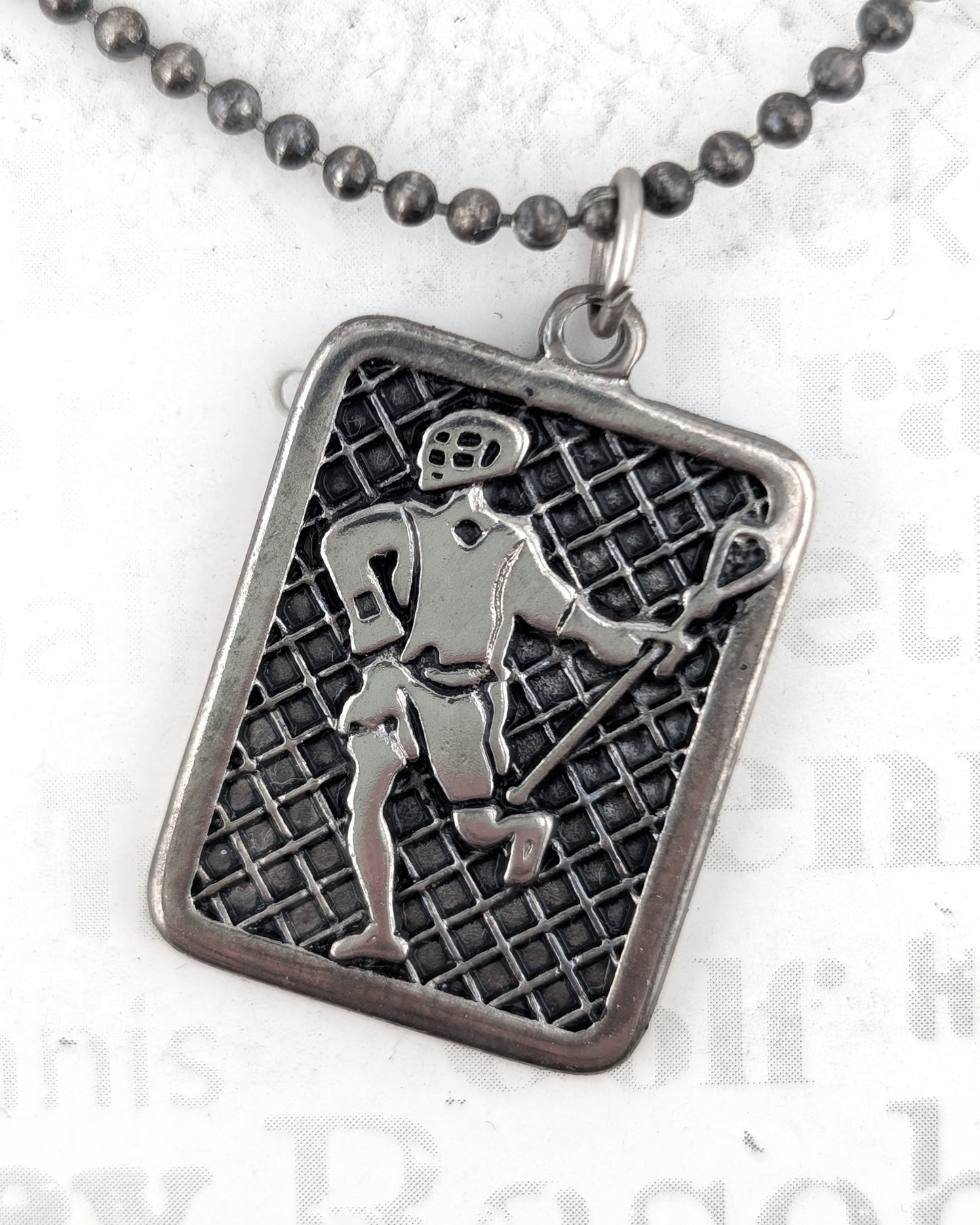 Silver pendant with a grid pattern and figure on a white background