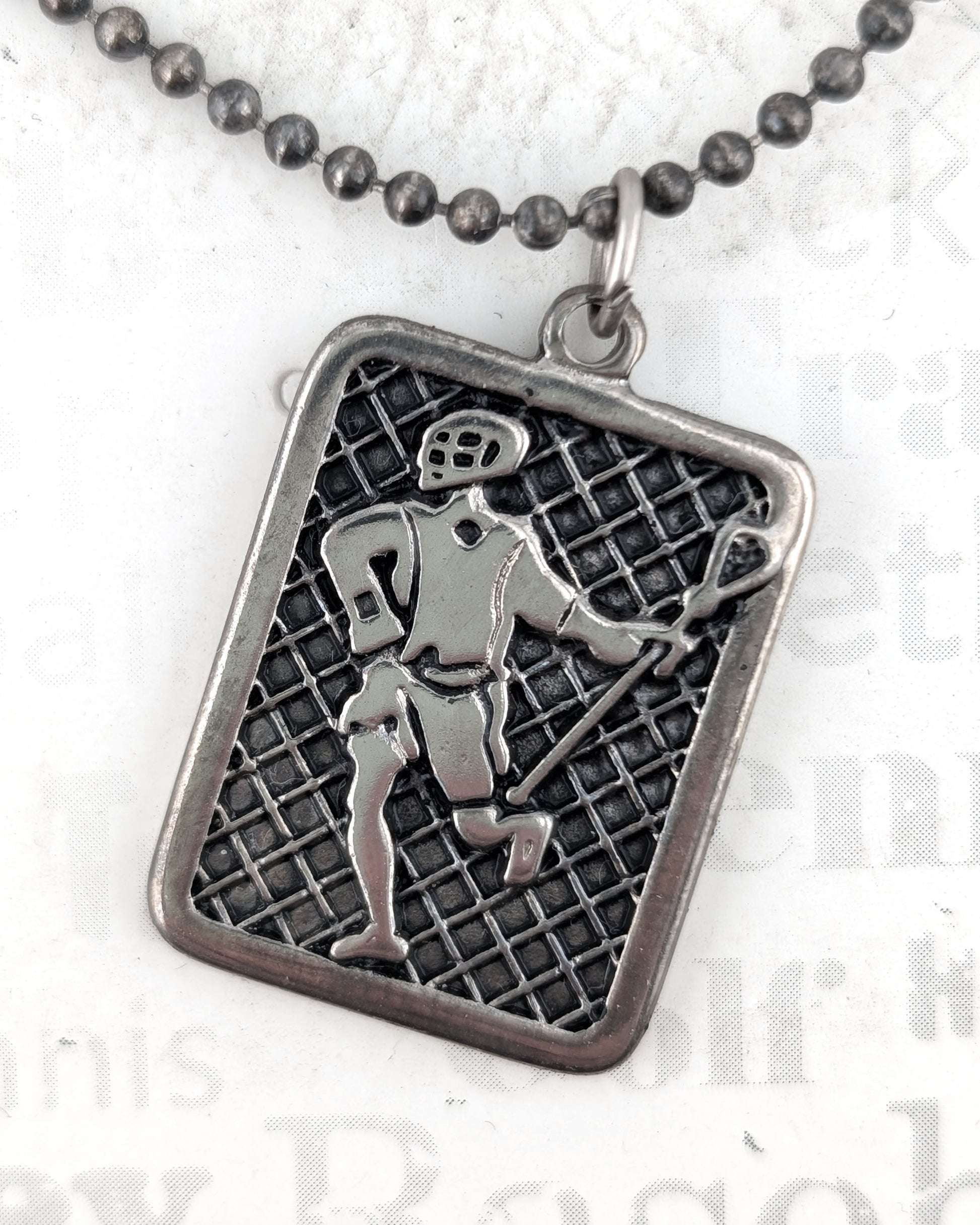 Silver pendant with a grid pattern and figure on a white background