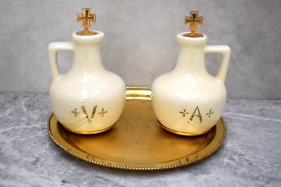 Two white ceramic bottles with gold crosses on a gold tray against a gray background