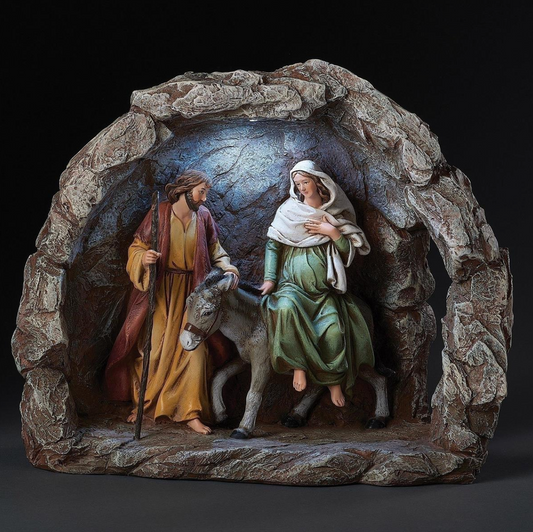 A nativity-style cave display sculpture showing Mary on a donkey and Joseph with a staff inside a rocky cave setting, photographed against a dark studio background.