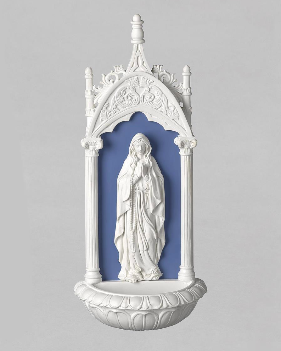 A white Gothic-style wall niche sculpture featuring a white statue of the Virgin Mary with rosary, set against a blue recessed background, photographed on a neutral gray studio background.