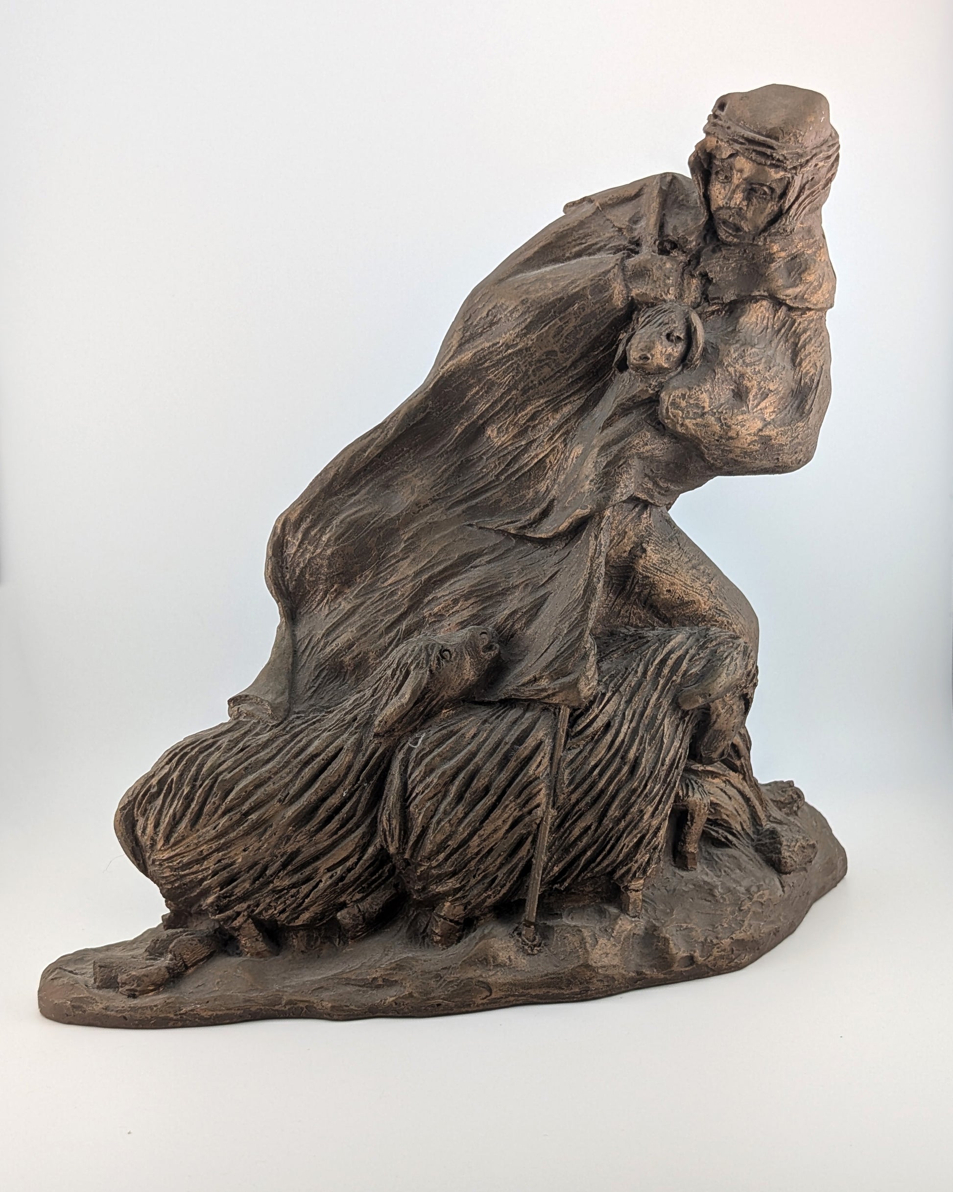 Bronze sculpture of a seated figure with long hair on a white background