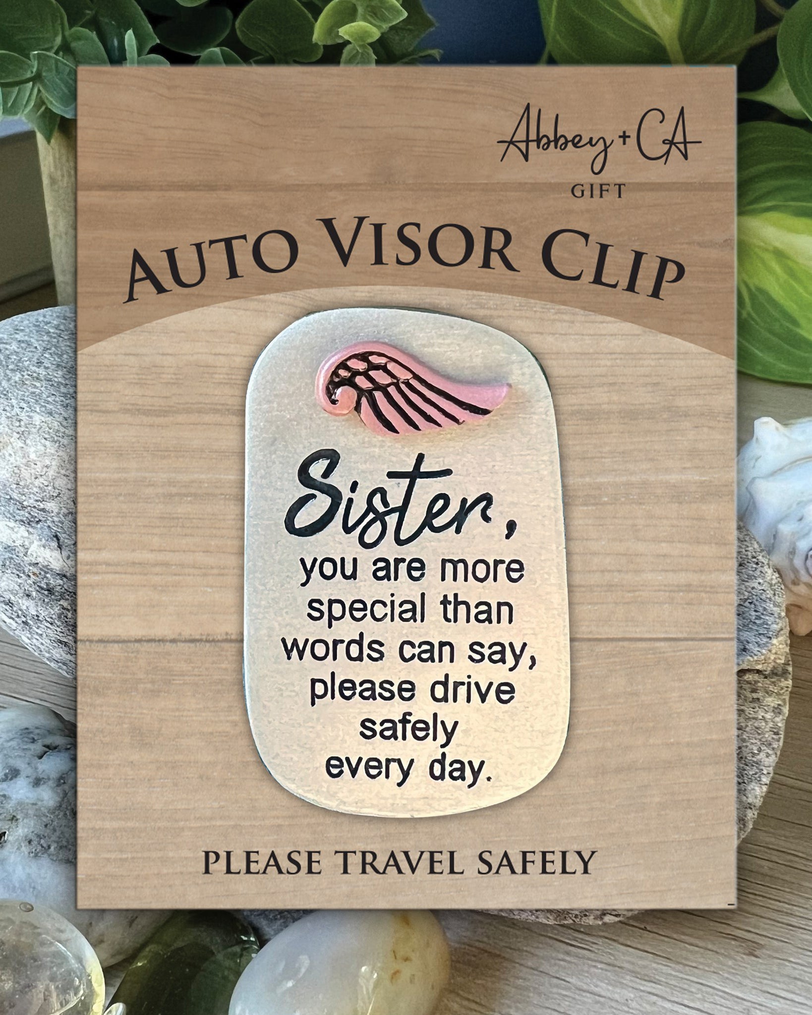 Wooden auto visor clip with a message for a sister, placed on a natural background.