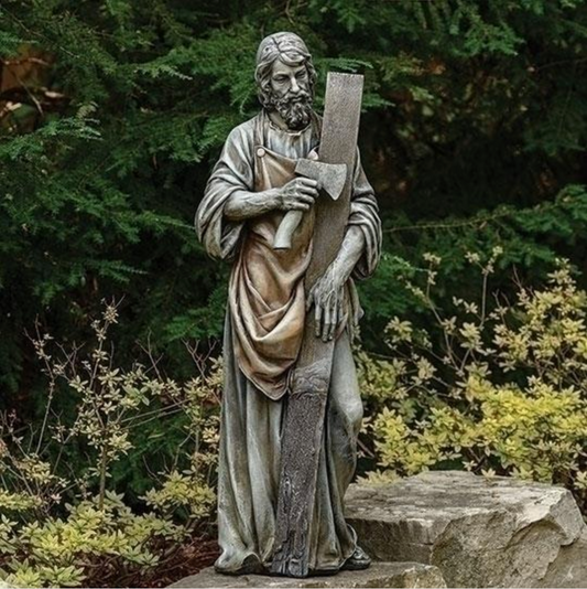 Statue of a religious figure holding a book in a garden setting