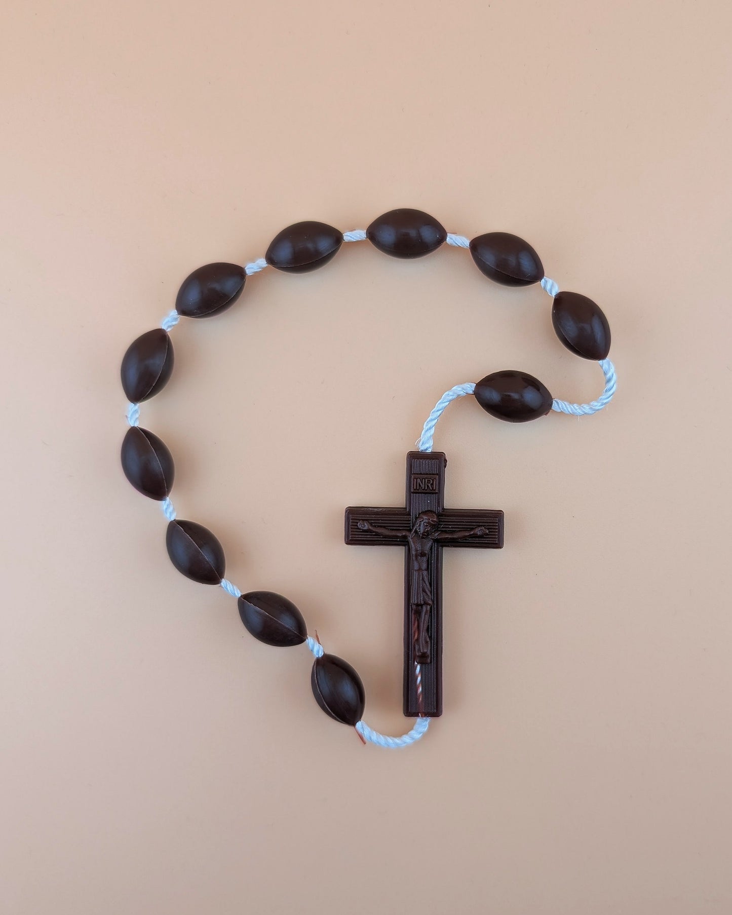 Plastic rosary with dark brown beads and a cross on a beige background