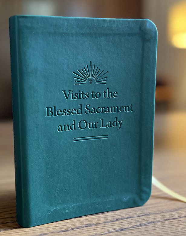Teal notebook with 'Visits to the Blessed Sacrament and Our Lady' text on a wooden surface.