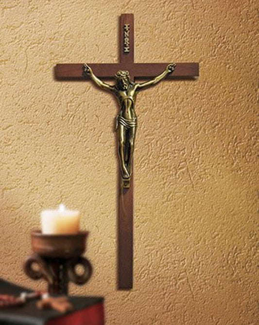 Wooden cross with a bronze figure of Jesus on a beige wall, next to a candle holder with a lit candle.